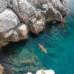 View from the rock cliffs of kayaker exploring the crystal clear Mediterranean waters of a cove off the coast of Dubrovnik, Croatia